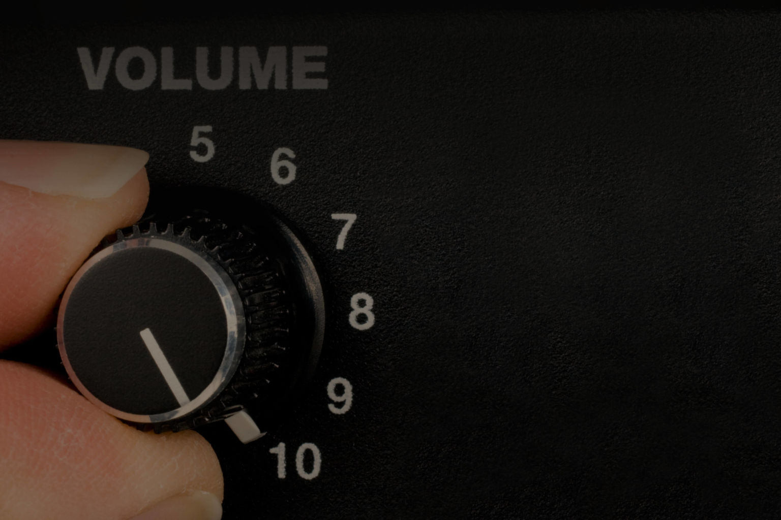 A hand turning an amplifier's volume knob up to ten