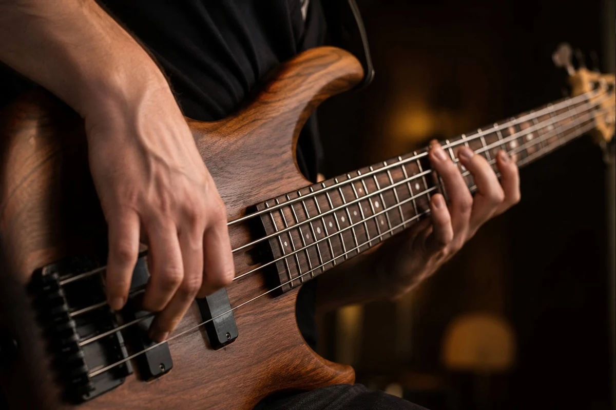 Close-up of a man's hands playing a natural walnut-finish electric bass